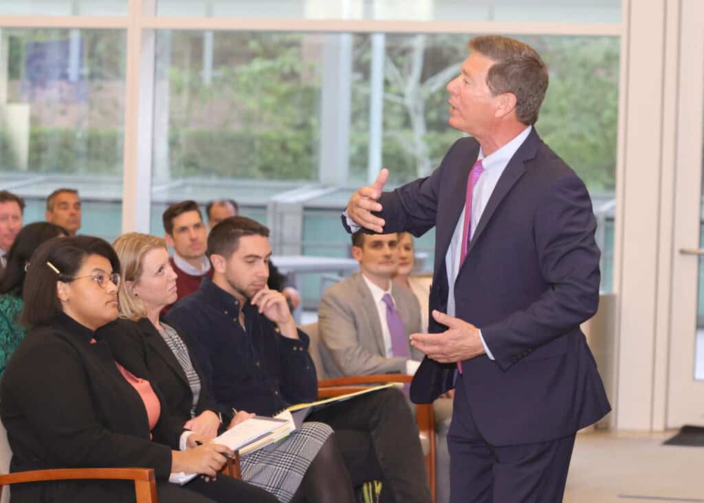 A man in a suit gives a lecture in front of a group of lawyers
