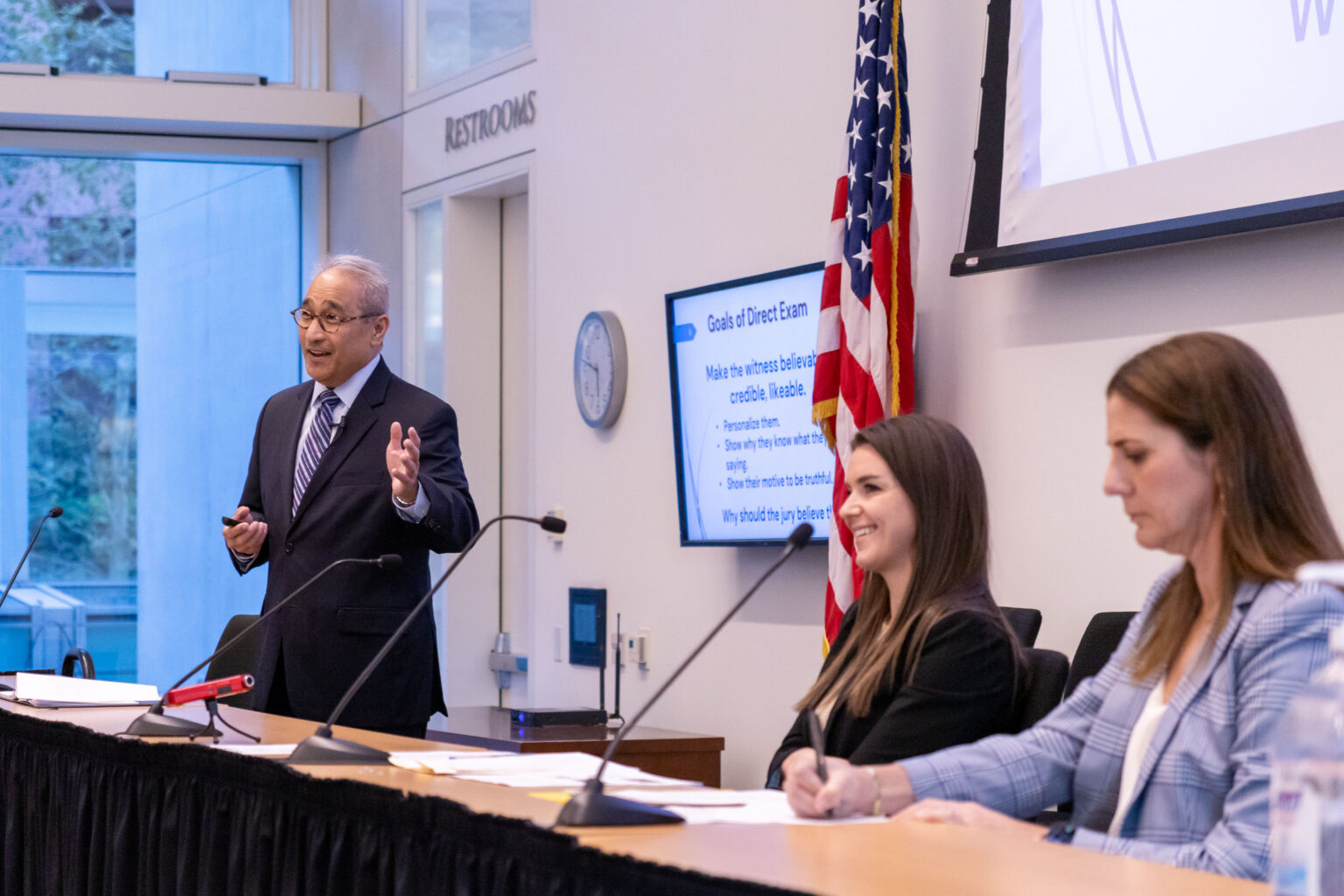 Judge Cumba and two attorneys lecturing on stage during a Trial Program event.
