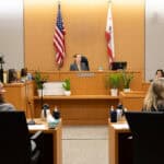 A courtroom with attorneys at desks, a judge, and a witness.