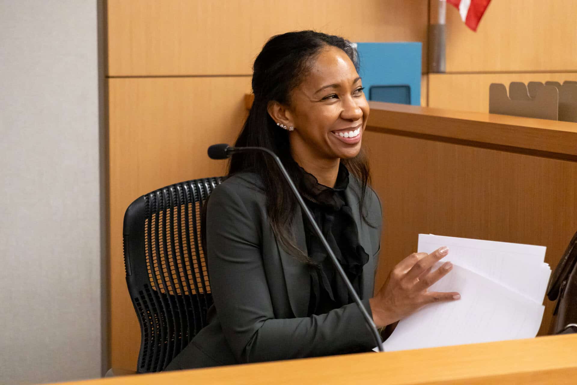 A woman smiling and holding papers at a desk in a courtroom